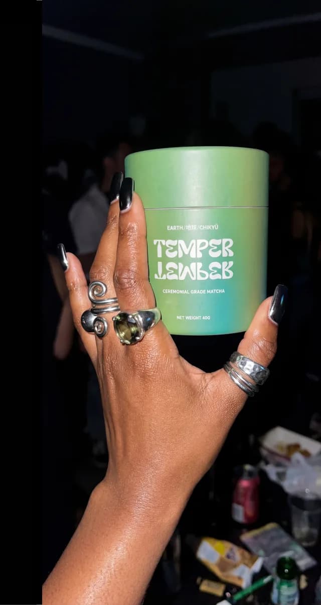 Hand with silver rings holding an Earth matcha tube